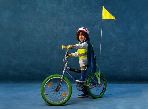 Jongentje met helm en cape op een fiets met een vlaggetje achterop