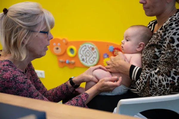 Medewerker van de GGD zet een vaccinatie bij een baby in het bovenbeen