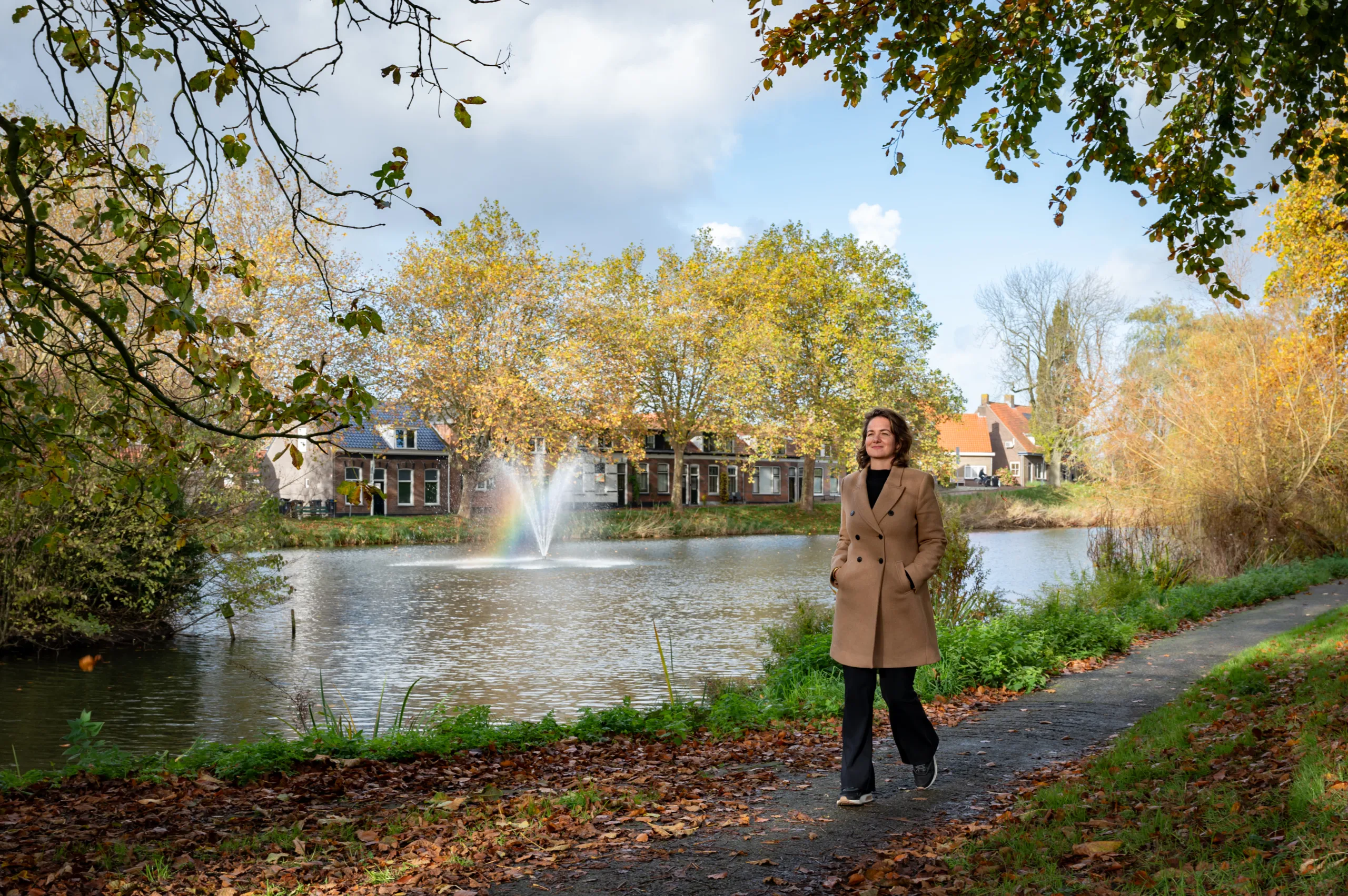 Dame die door de natuur wandelt in Goes. Op de foto water met een fontein omringd door bomen.